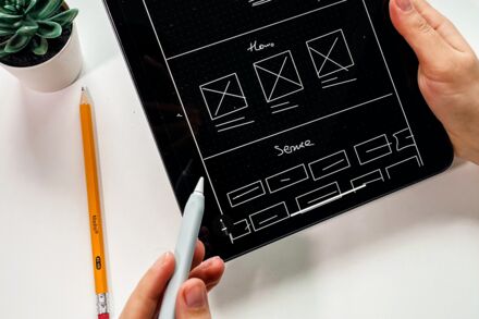 Bild zeigt eine Hand mit Stift die auf Skizzen-Wireframes einer Webseite zeigt.